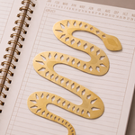 Marcapáginas metálico con forma de serpiente dorada colocado sobre un cuaderno.
