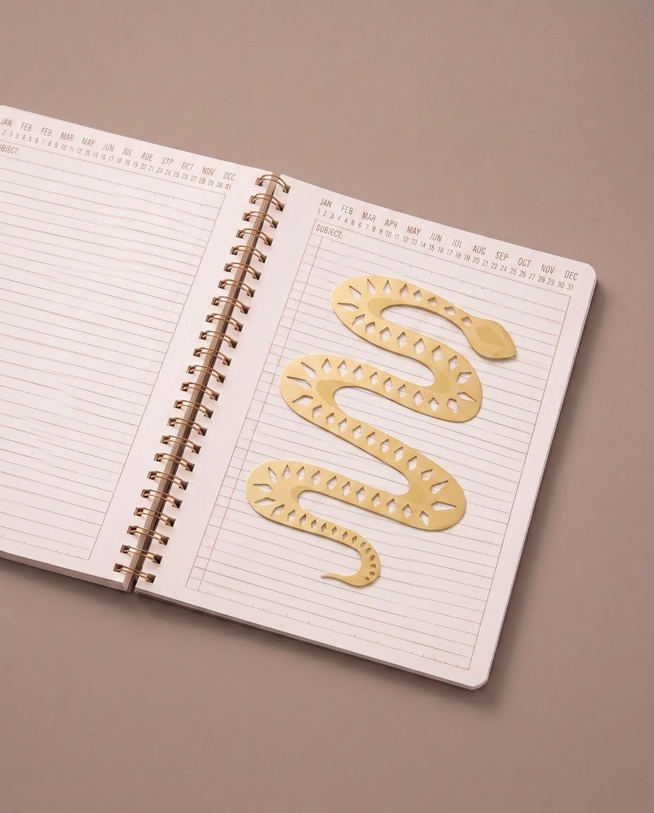 Marcapáginas metálico con forma de serpiente colocado entre las páginas de un cuaderno abierto.