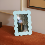 Marco de fotos azul de MDF con borde ondulado, colocado sobre un banco tapizado en terciopelo