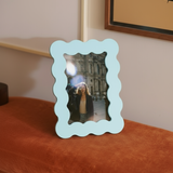 Marco de fotos azul de MDF con borde ondulado, colocado sobre un banco tapizado en terciopelo