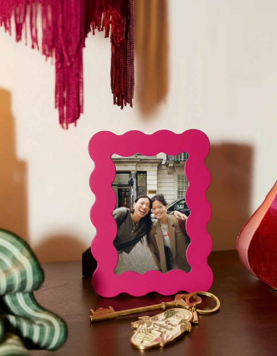 Marco de fotos rosa de MDF colocado en un mueble junto a una lámpara naranja y llaves decorativas