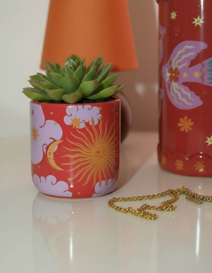 Detalle del mini macetero de cerámica con estampado celestial en tonos rojos y lilas.