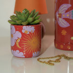 Detalle del mini macetero de cerámica con estampado celestial en tonos rojos y lilas.