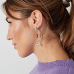 Modelo con pendientes plateados con charms coloridos en forma de aro grande.

