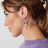 Modelo con pendientes plateados con charms coloridos en forma de aro grande.

