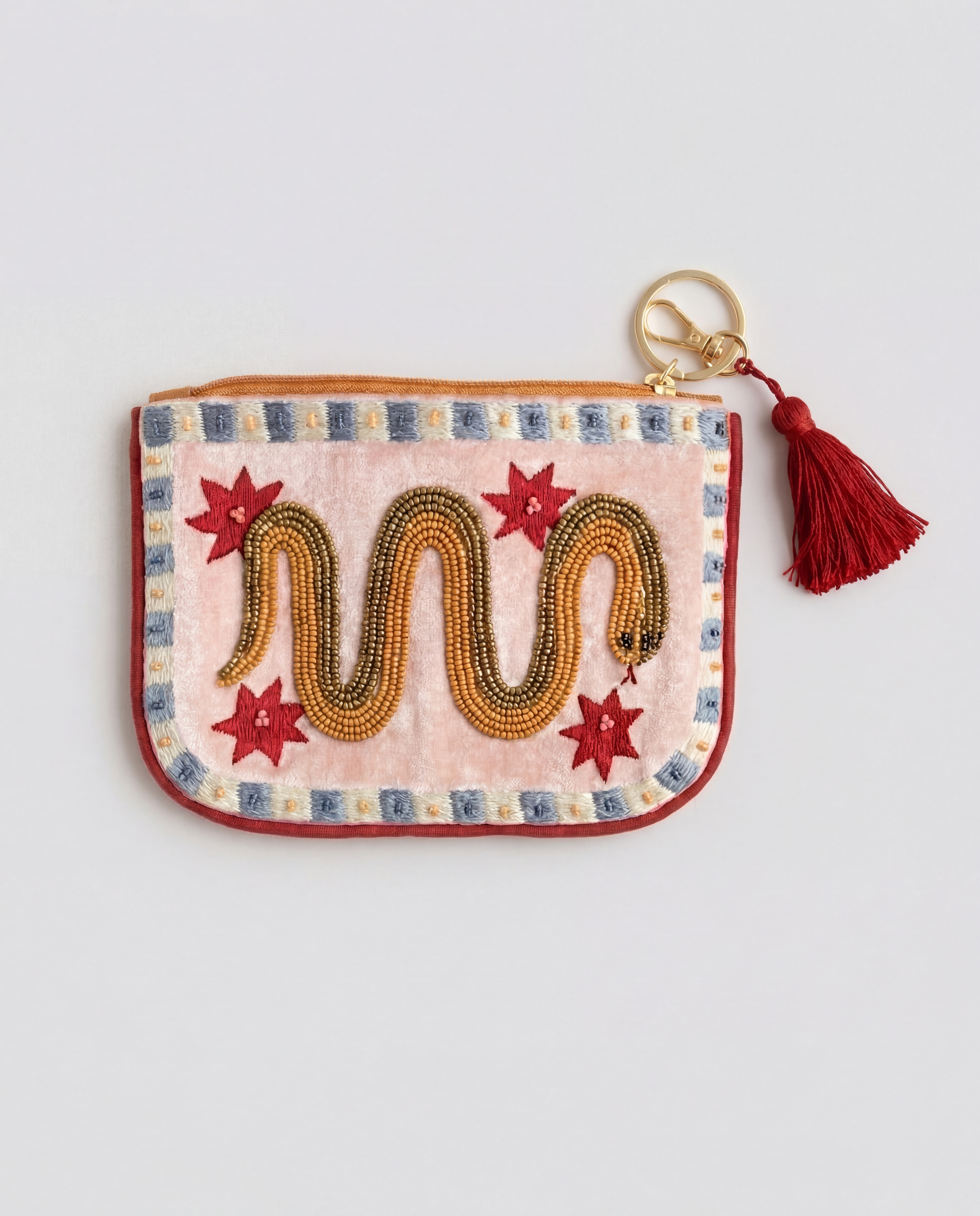 Vista frontal de monedero bordado con serpiente dorada, estrellas rojas, cremallera y borla.