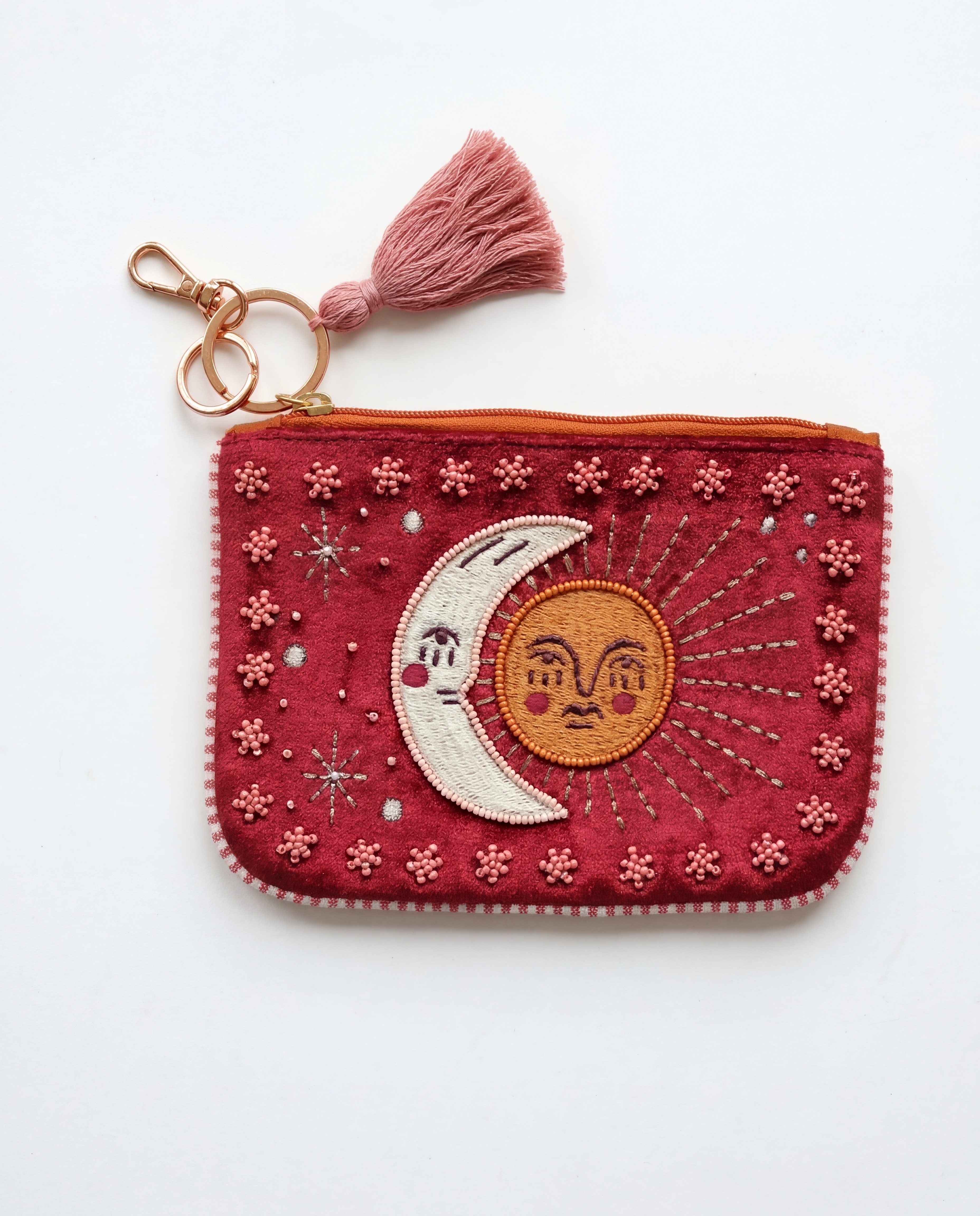 Monedero granate con sol dorado, luna blanca, estrellas bordadas y borla rosa.