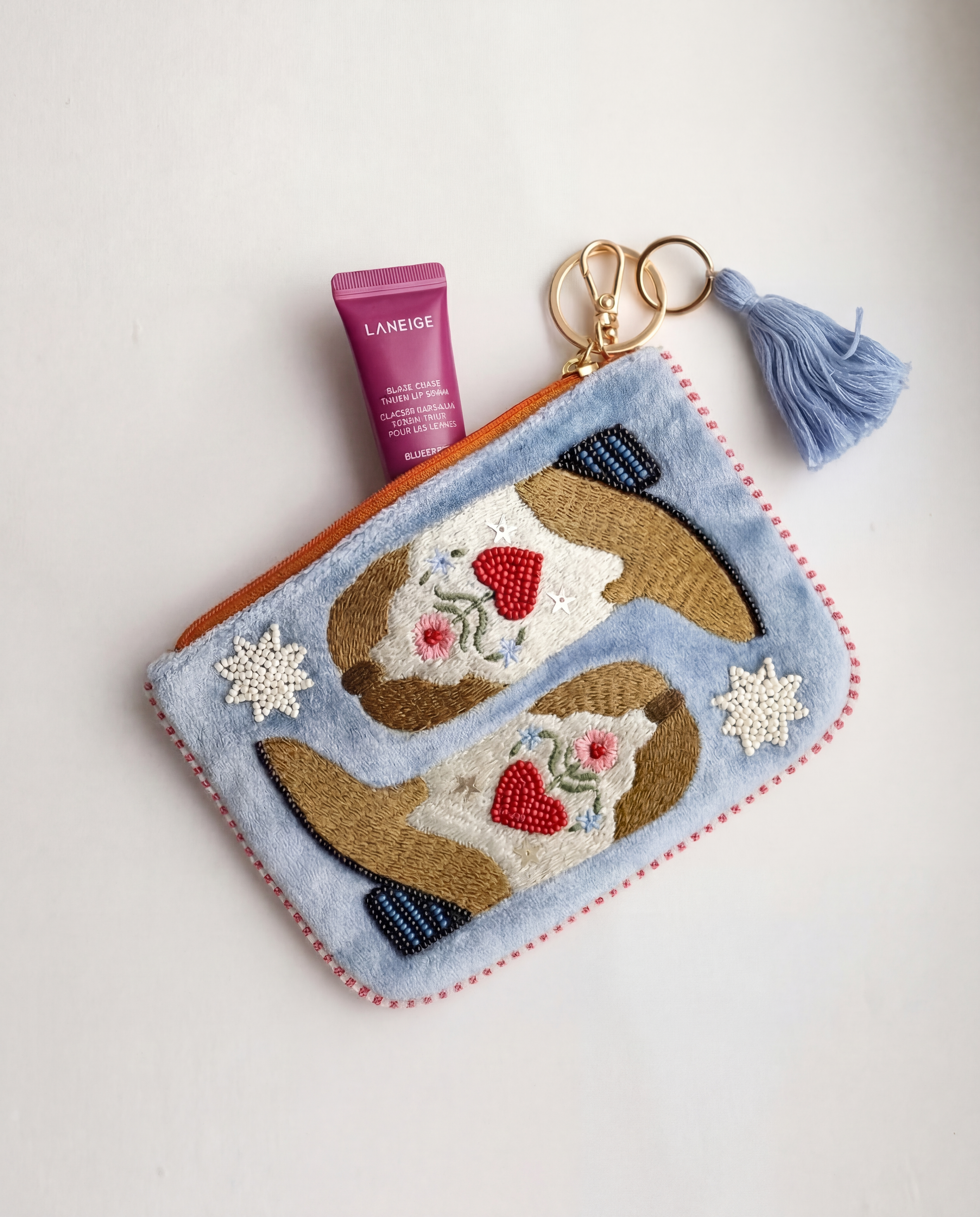 Monedero azul pastel con dos botas cowboy marrones, flores bordadas y abalorios.