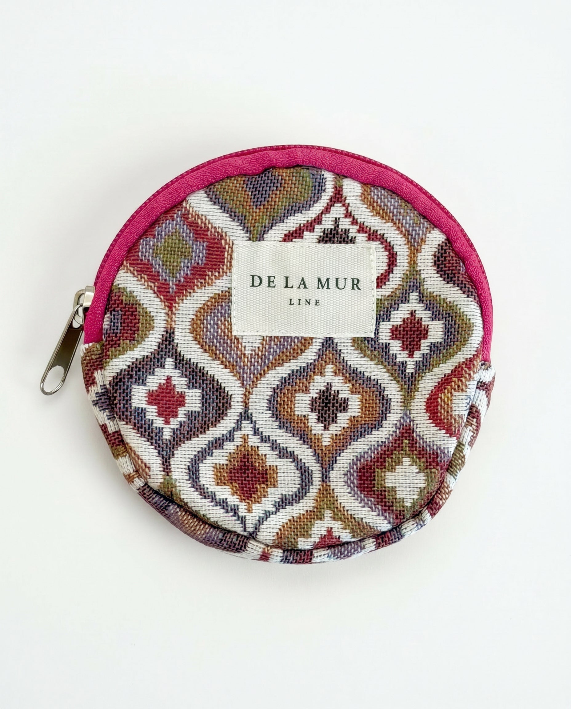 Monedero redondo de jacquard con estampado geométrico en tonos rosa, lila y beige.