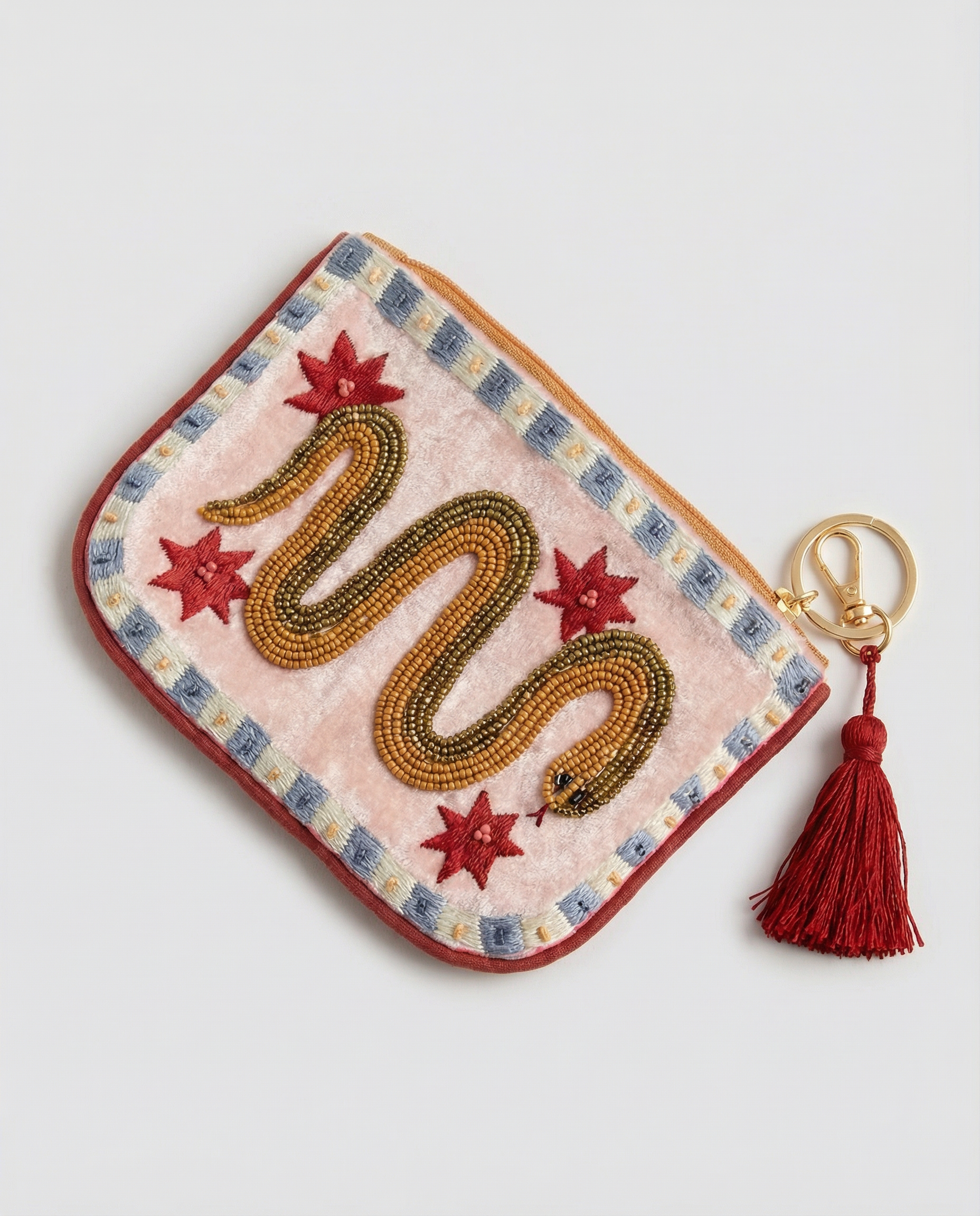 Monedero crema con serpiente dorada bordada, estrellas rojas y borla granate, vista diagonal.