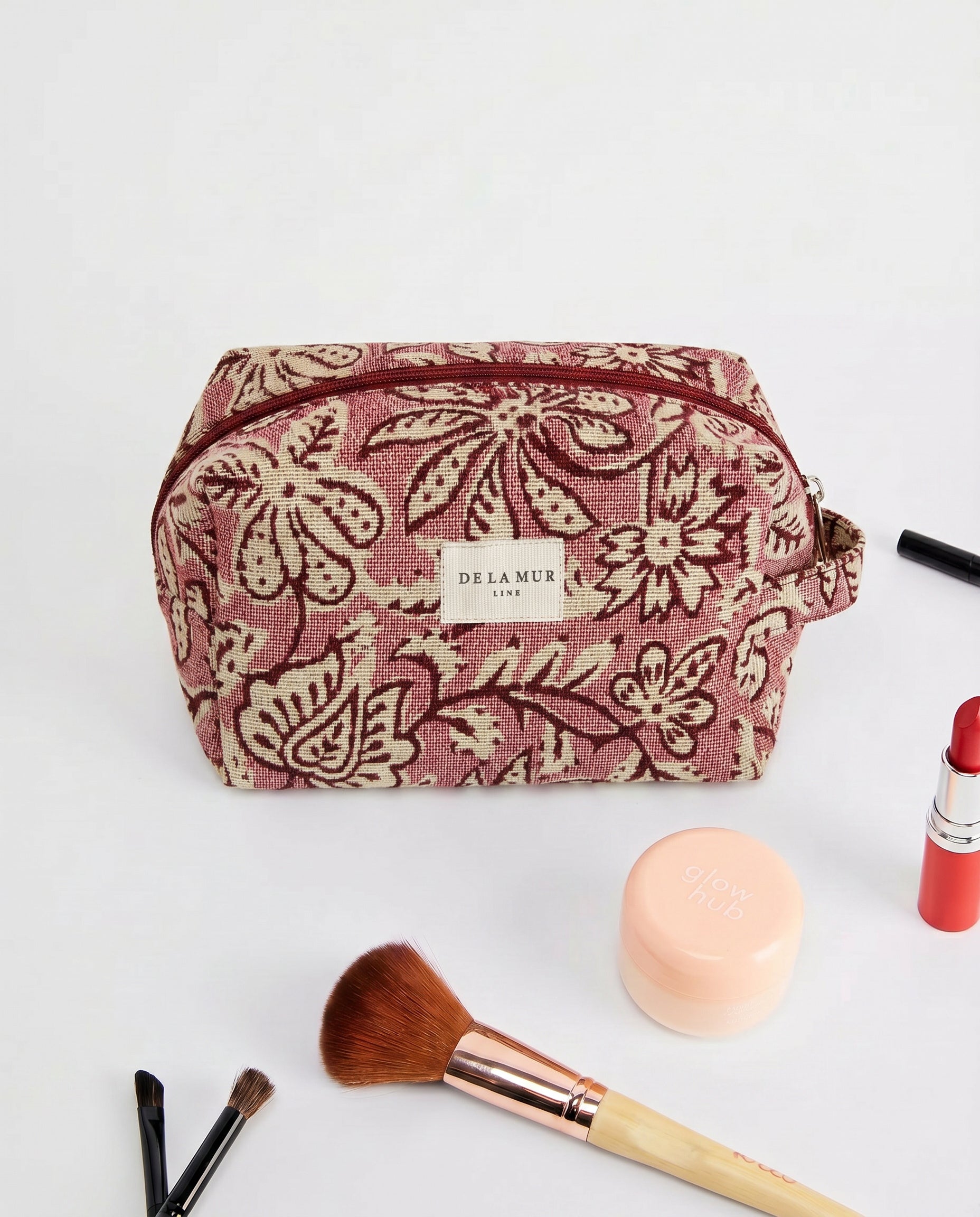 Neceser de jacquard floral con brochas y productos de maquillaje alrededor.