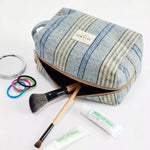 Neceser de jacquard de rayas azules con productos de maquillaje alrededor.
