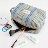 Neceser de jacquard de rayas azules con productos de maquillaje alrededor.