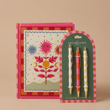 Pack de cuaderno de tapa dura Soles A Dopo junto a un set de tres bolígrafos ilustrados.