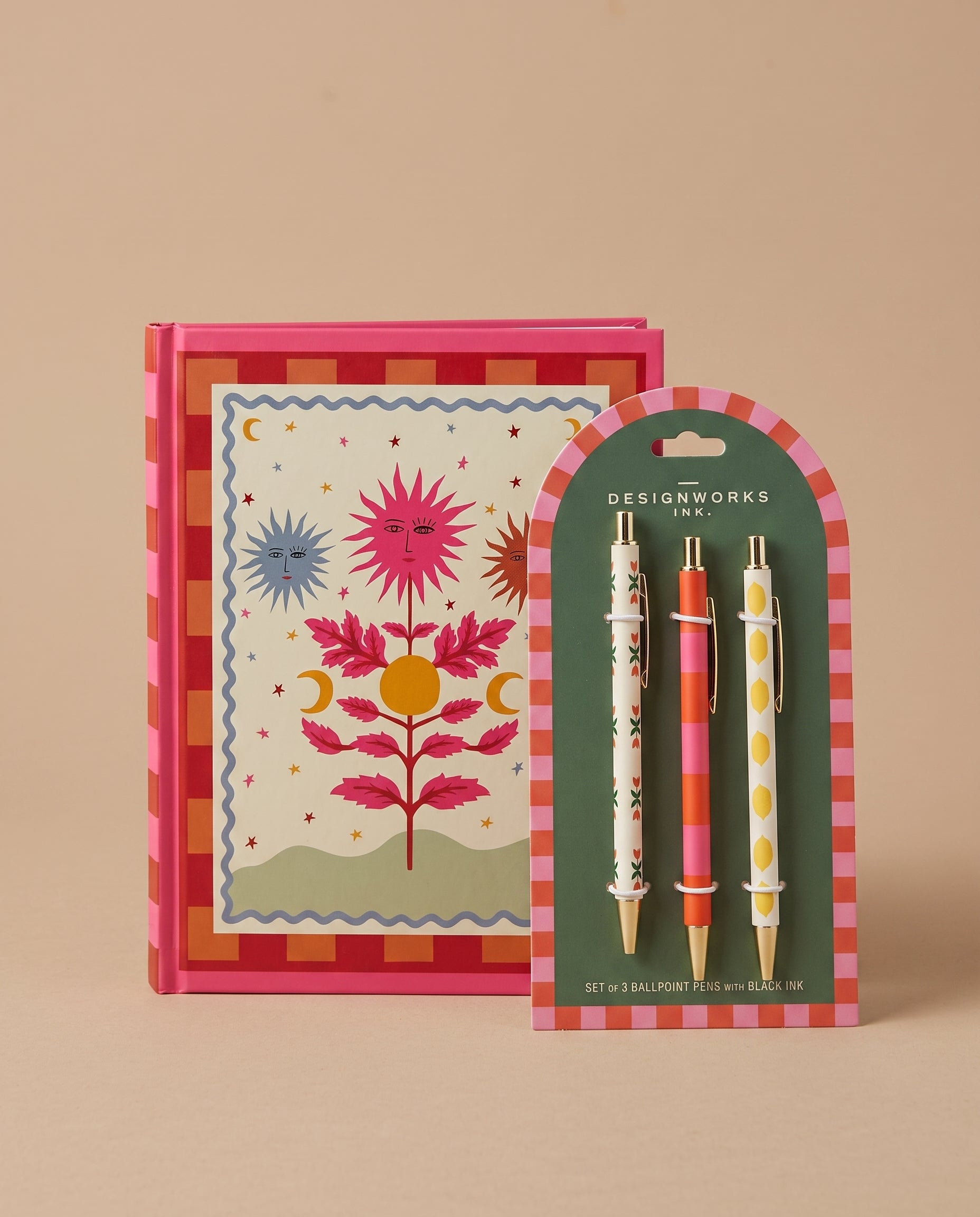 Pack de cuaderno de tapa dura Soles A Dopo junto a un set de tres bolígrafos ilustrados.