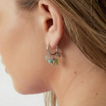 Pendientes plateados con aro y charms coloridos en la oreja de una modelo, vista lateral.