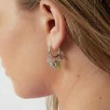 Pendientes plateados con aro y charms coloridos en la oreja de una modelo, vista lateral.