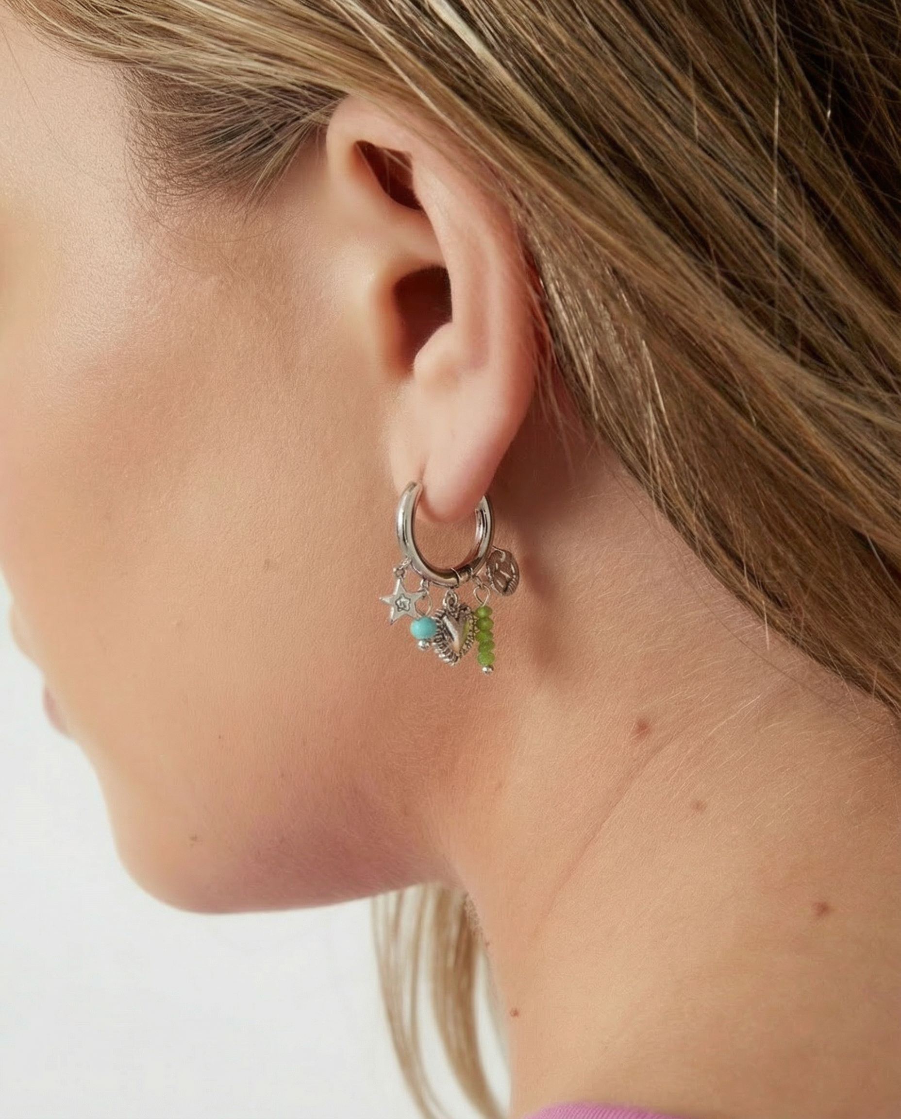 Pendientes plateados con aro y charms coloridos en la oreja de una modelo, vista lateral.