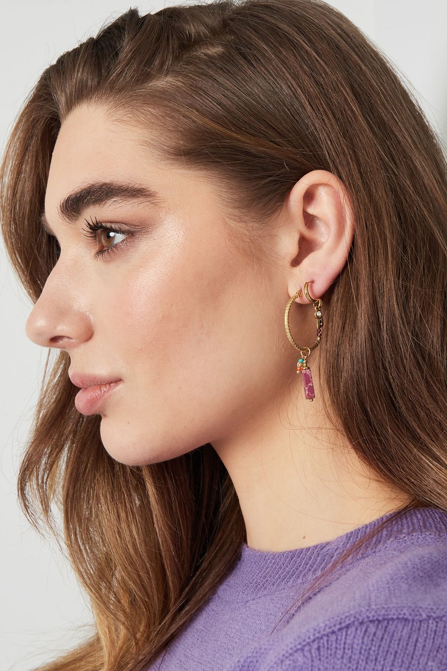 Mujer con pendientes dorados de aro con piedra rosa y perla colgante.