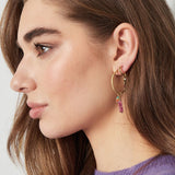 Mujer con pendientes dorados de aro con piedra rosa y perla colgante.