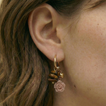 Pareja de pendientes dorados con charms bohemios y rosa en relieve, vista frontal.