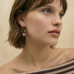 Pendientes de aro dorados con charms de rosa tallada y cuentas en tonos tierra sobre fondo blanco.