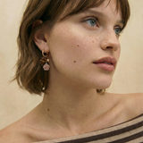 Pendientes de aro dorados con charms de rosa tallada y cuentas en tonos tierra sobre fondo blanco.