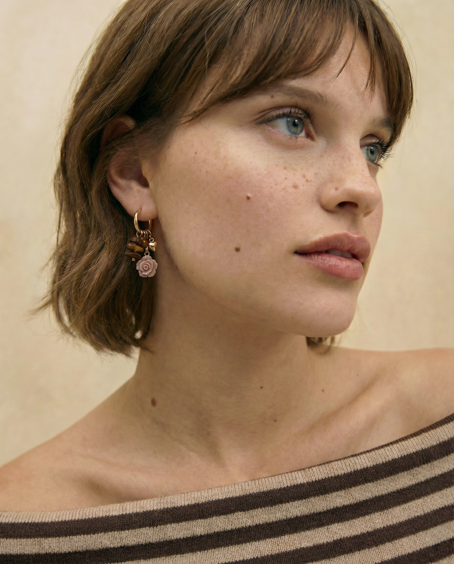 Pendientes de aro dorados con charms de rosa tallada y cuentas en tonos tierra sobre fondo blanco.