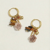 Pendientes de aro dorados con charms de rosa tallada y cuentas en tonos tierra sobre fondo blanco.