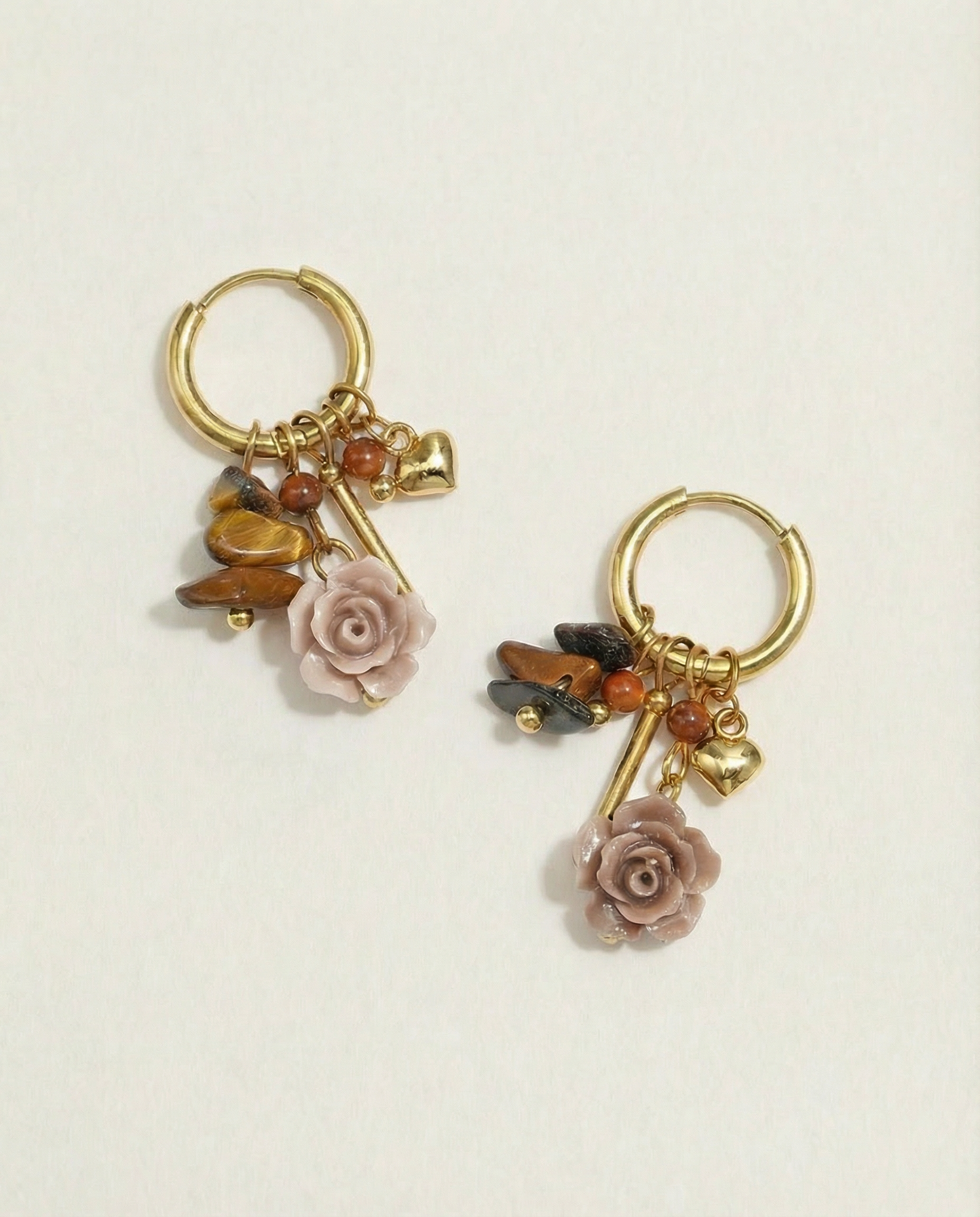 Pendientes de aro dorados con charms de rosa tallada y cuentas en tonos tierra sobre fondo blanco.