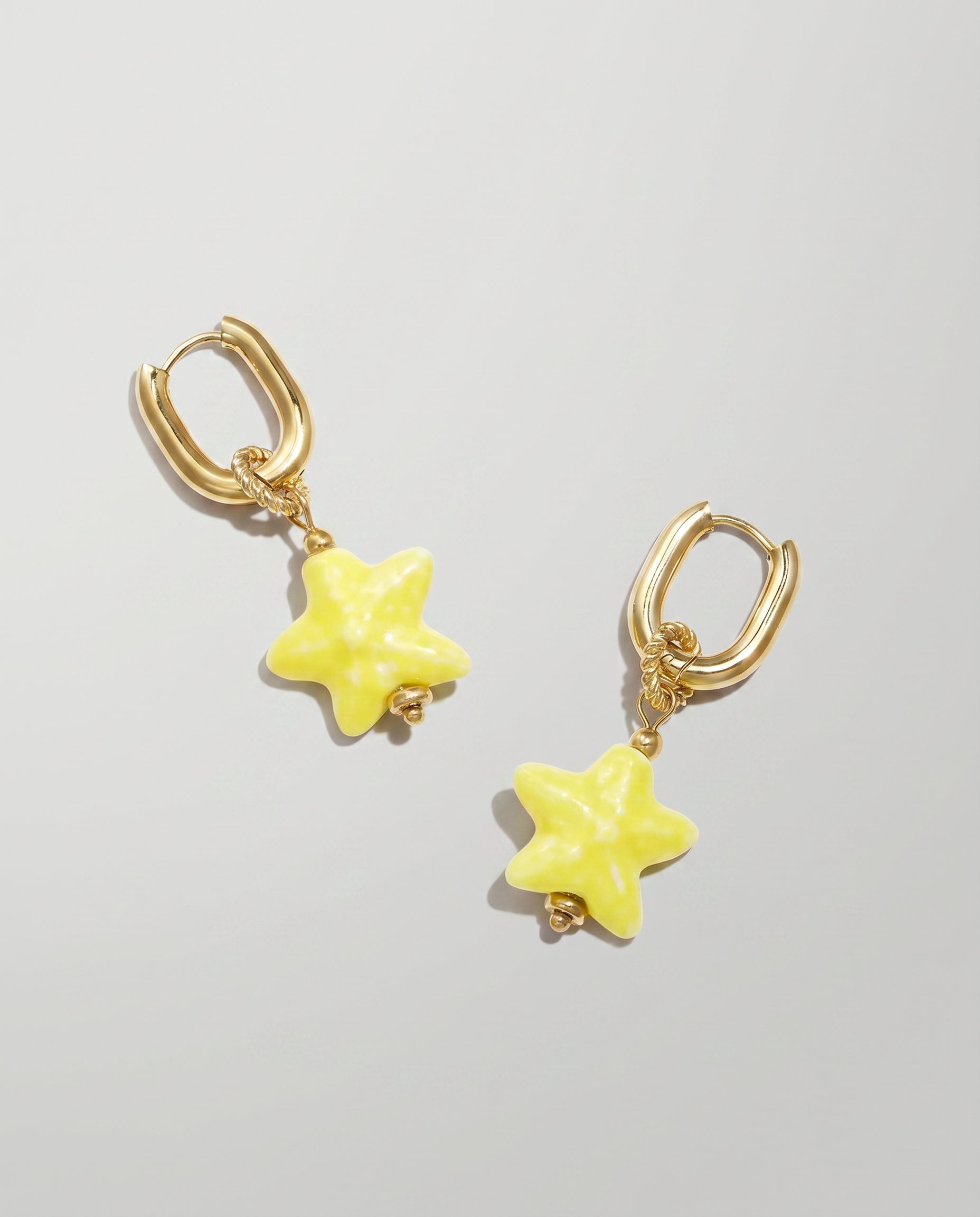 Pendientes de aro dorados con colgante de estrella amarilla de cerámica.
