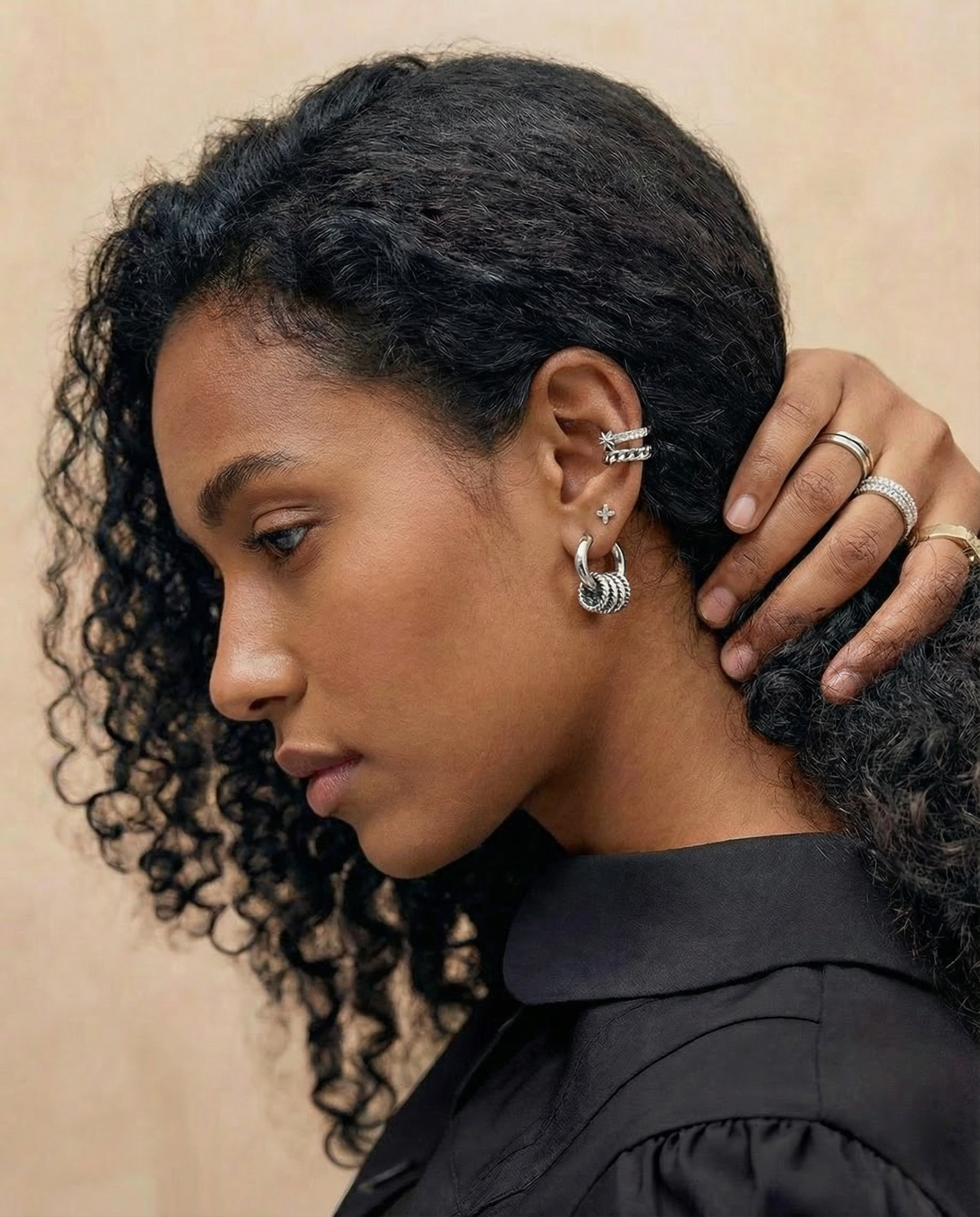 Pendientes plateados con aro y nudo texturizado en la oreja de una modelo de piel oscura y cabello rizado.