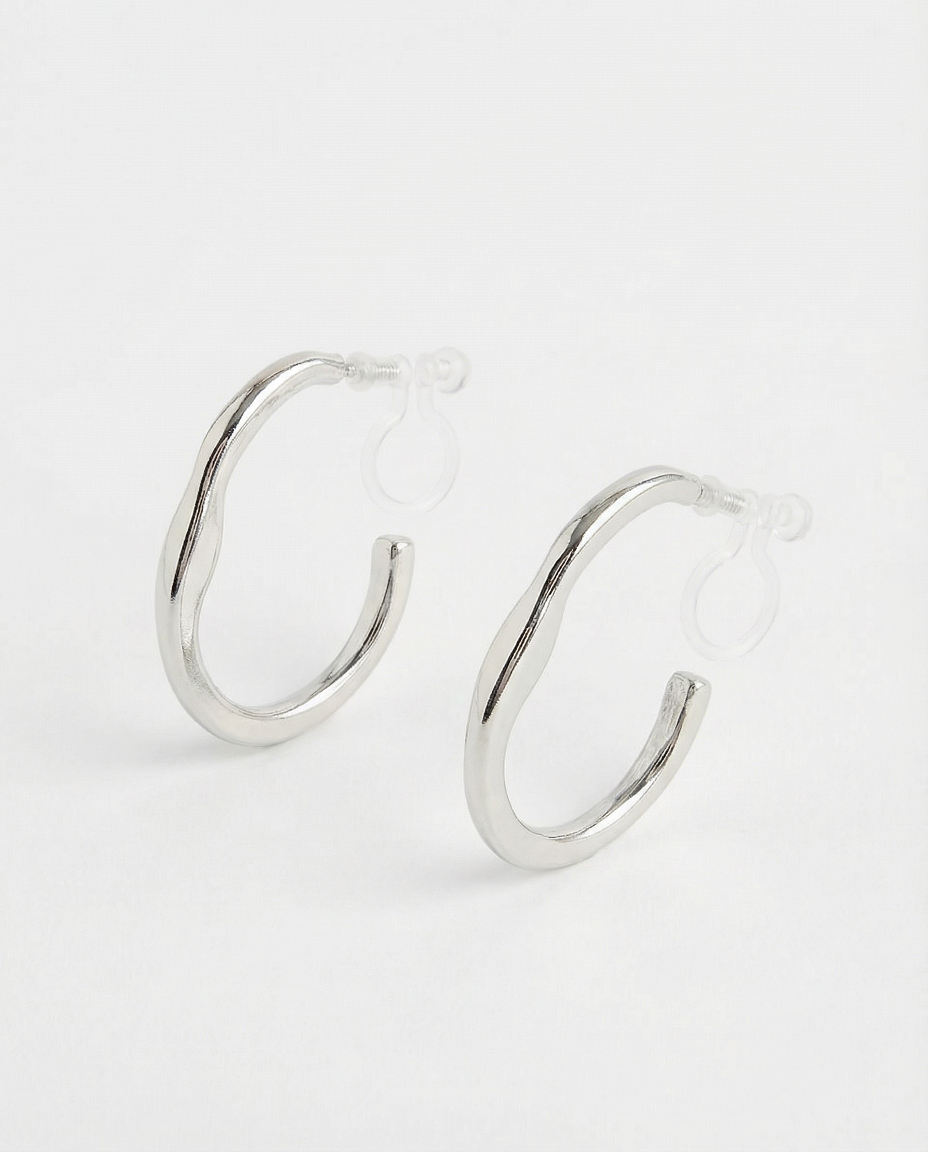 Detalle de pendientes plateados ondulados con sistema de clip en acero inoxidable.