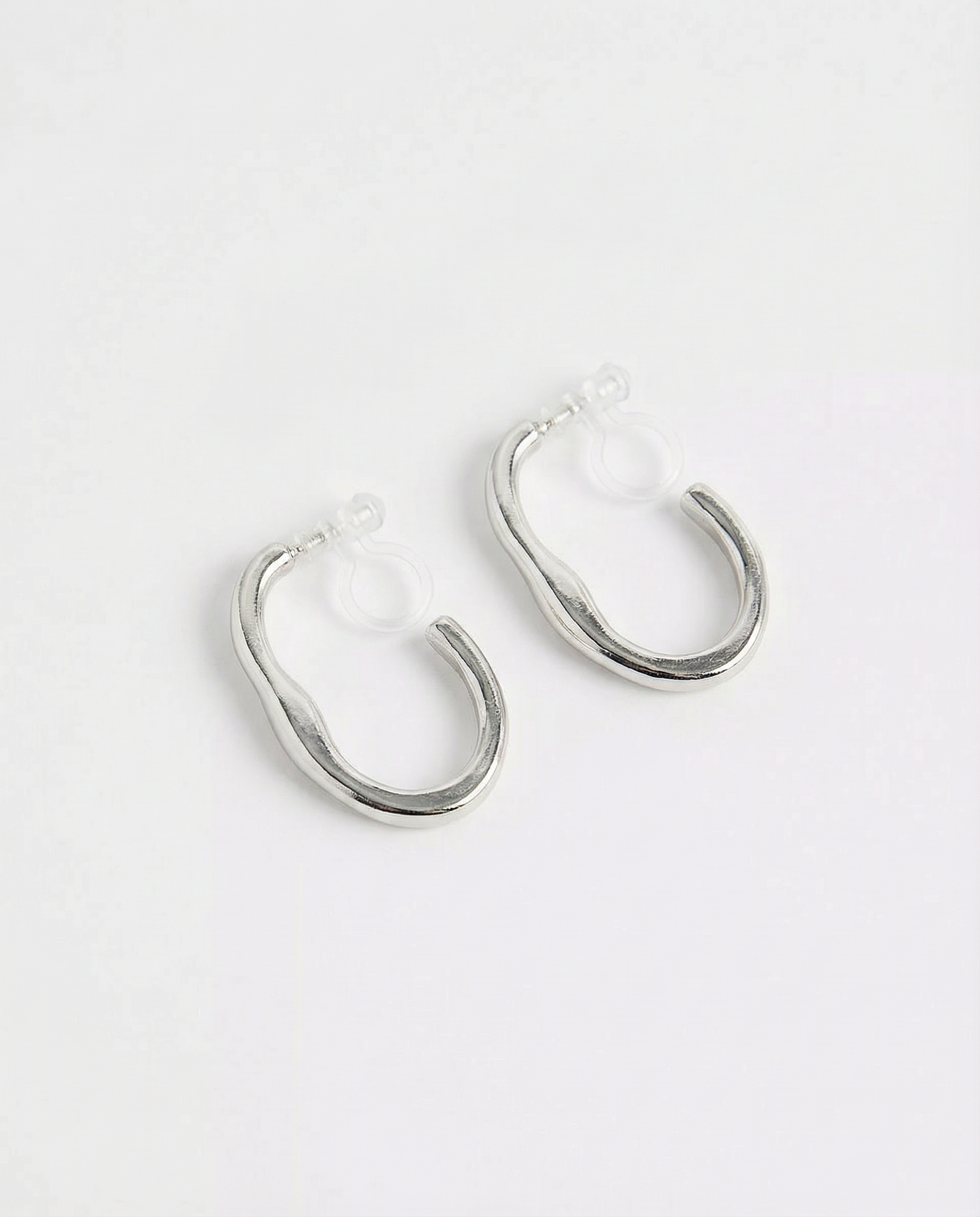 Pendientes de aro ondulado plateados con cierre de clip sobre fondo blanco, vista frontal.