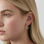 Pendientes plateados de aro ondulado con cierre de clip en la oreja de una modelo rubia, vista lateral.