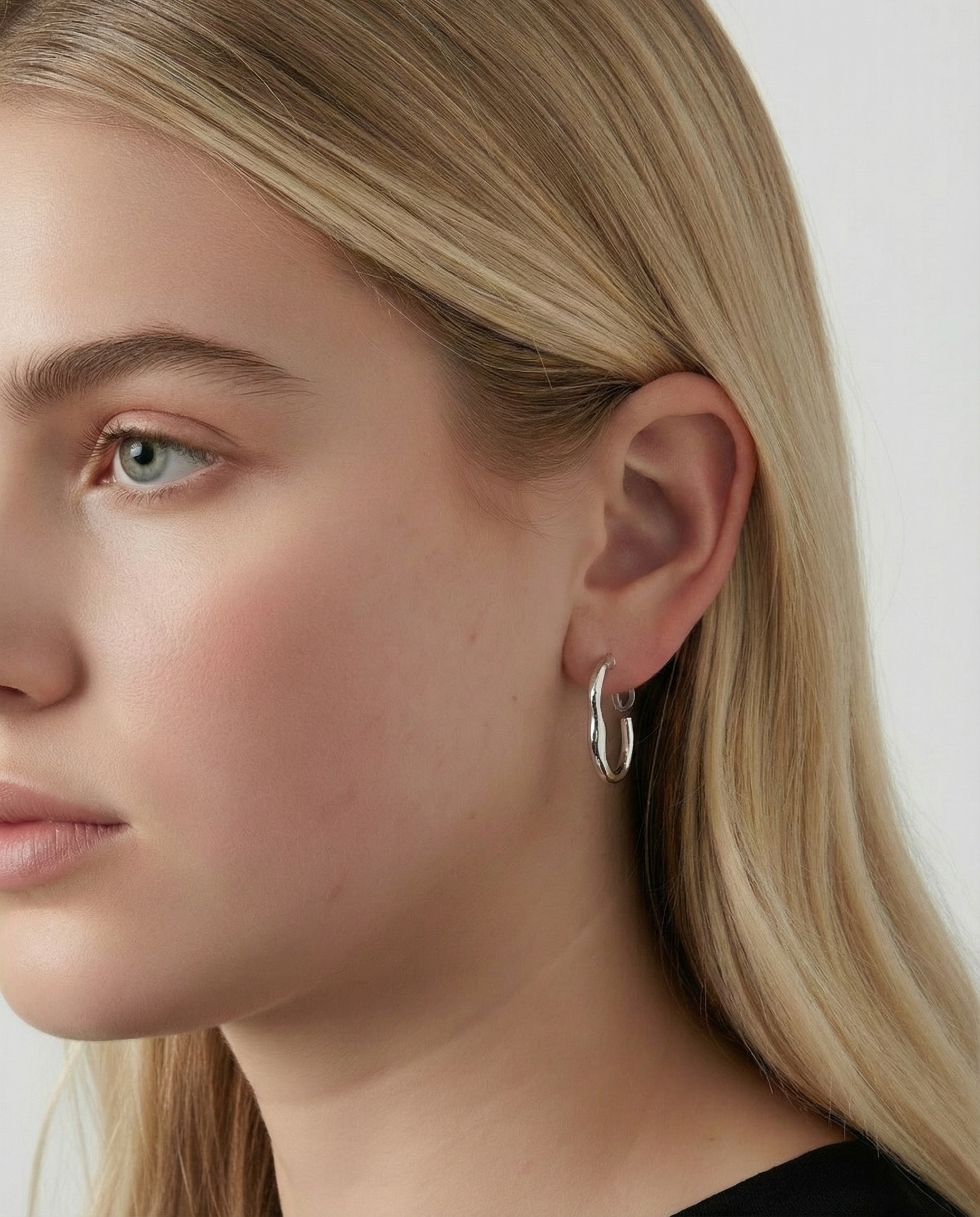 Pendientes plateados de aro ondulado con cierre de clip en la oreja de una modelo rubia, vista lateral.