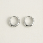 Detalle de pendientes plateados minimalistas en forma de aro curvado.