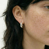 Pendientes plateados tipo aro con diseño curvado sobre fondo blanco.