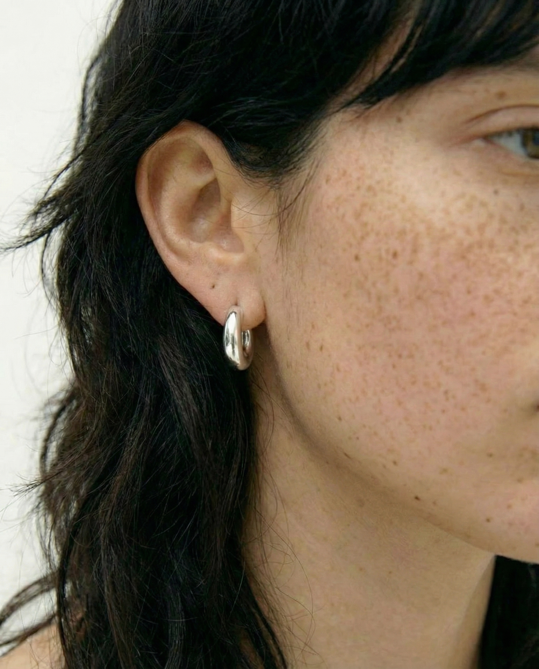 Pendientes plateados tipo aro con diseño curvado sobre fondo blanco.