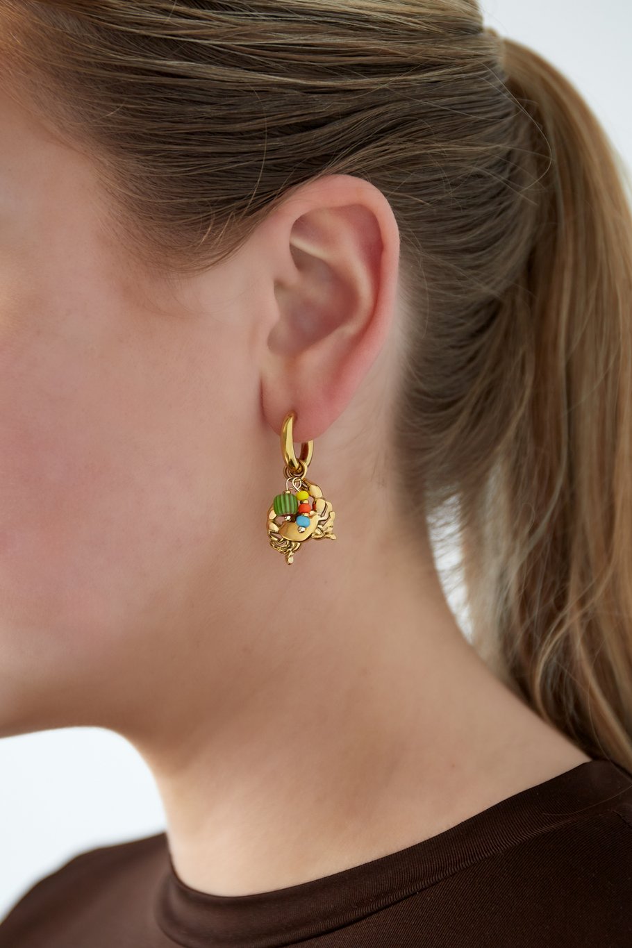 Mujer con pendientes de aro dorado con charm de cangrejo y abalorios

