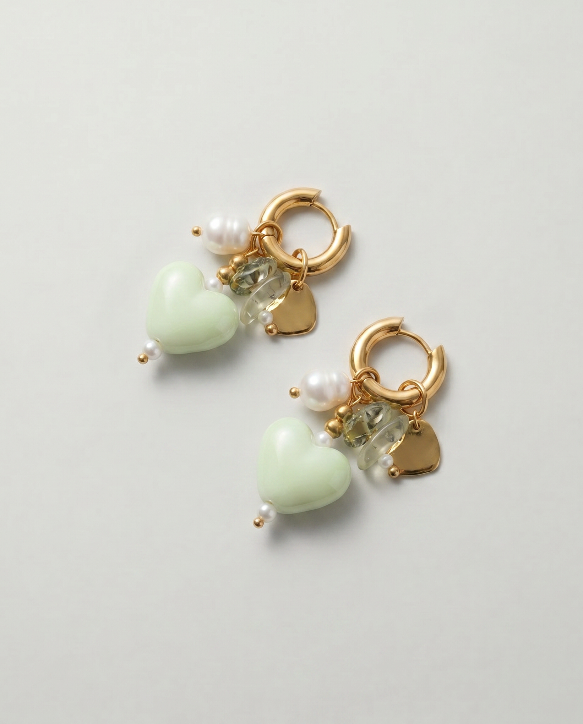 Pendientes de acero inoxidable con corazón de cerámica verde, perla y cristal sobre fondo blanco.