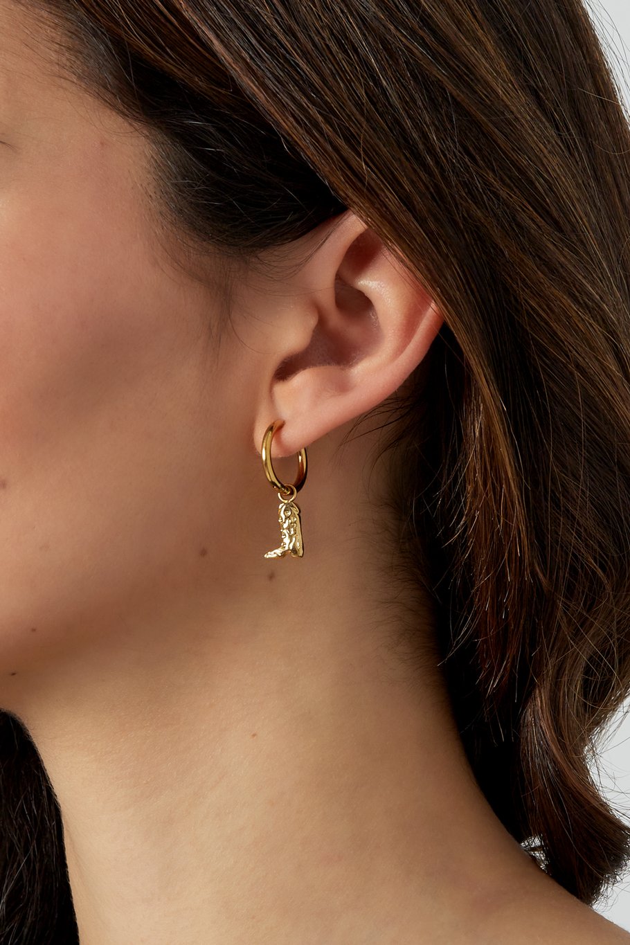 Detalle de pendientes dorados con colgante de bota estilo western, en primer plano