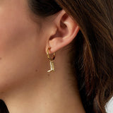 Detalle de pendientes dorados con colgante de bota estilo western, en primer plano