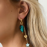 Pareja de pendientes dorados con corazón verde y estrella tipo ojo, diseño llamativo y colorido.