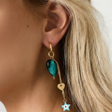 Pareja de pendientes dorados con corazón verde y estrella tipo ojo, diseño llamativo y colorido.