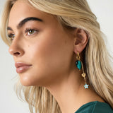 Detalle de pendientes con corazón verde brillante, cadena dorada y charm de estrella azul.