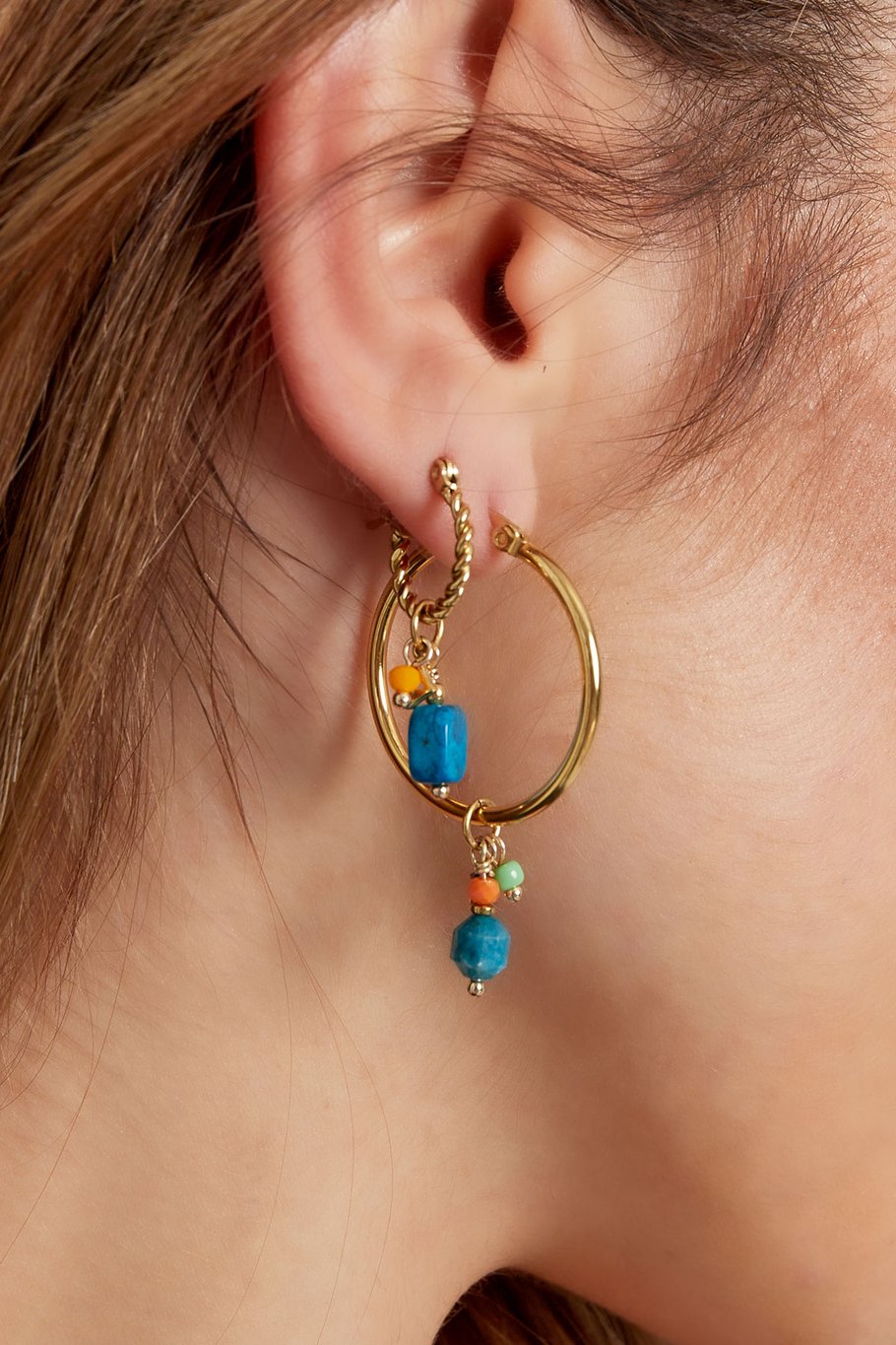 Pendientes boho de aro pequeño dorado con charm colgante azul, puestos en oreja.

