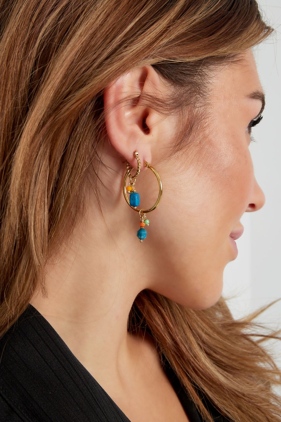 Modelo con pendientes dorados y piedra azul combinados con aro dorado grande.
