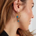 Modelo con pendientes dorados y piedra azul combinados con aro dorado grande.