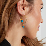 Modelo con pendientes dorados y piedra azul combinados con aro dorado grande.